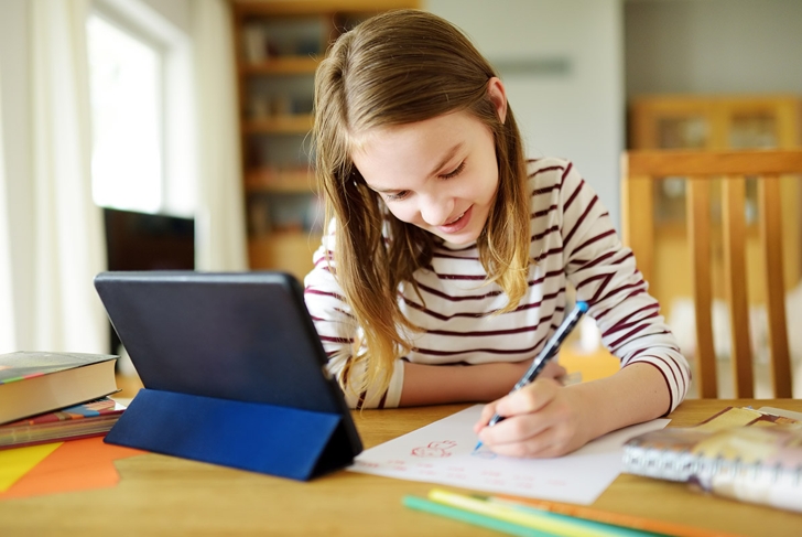 Preteen schoolgirl doing her homework with digital tablet at home. Child using gadgets to study. Education and distance learning for kids. Homeschooling during quarantine. Stay at home entertainment.