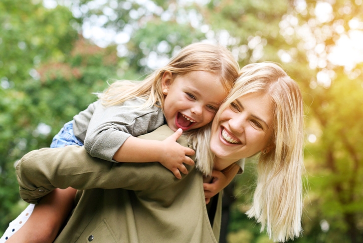 Cute young daughter on a piggy back ride with her mother.