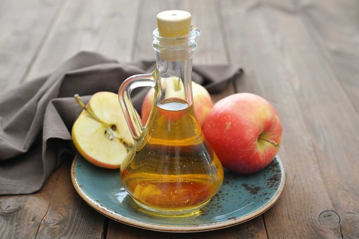 Apple cider vinegar in glass bottle and fresh apples on wooden background