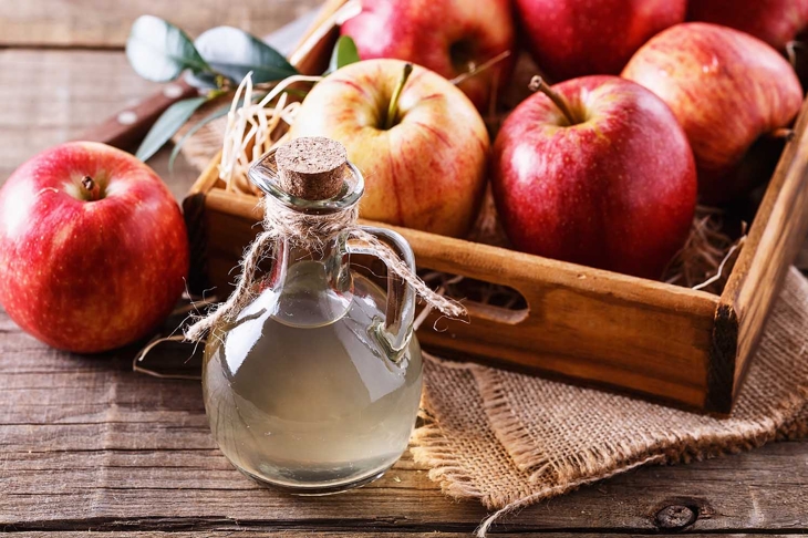 Bottle of unfiltered apple cider vinegar and apples in a wooden box over rustic background close up